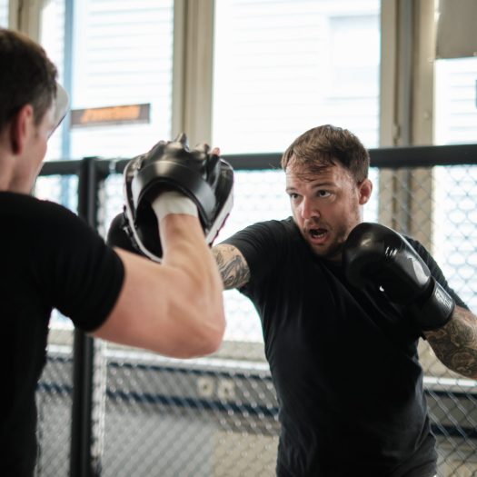 Hauzel Kampfsport Stuttgart Ludwigsburg Degerloch Möglingen MMA Krav Maga Gym Fitness Zentrum Selbstverteidigung Sporttraining Kampfperformance Kampfschule. Training für Erwachsene und Kinder – Sportlicher Mann trainiert mit Trainer im Gym und schlägt zu.