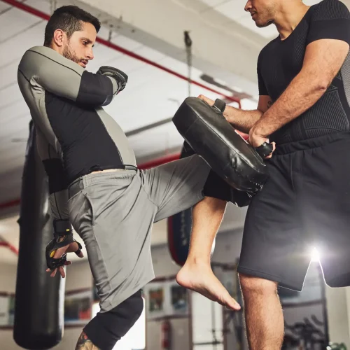 Hauzel Kampfsport Stuttgart Ludwigsburg Degerloch Möglingen MMA Krav Maga Gym Fitness Zentrum Selbstverteidigung Sporttraining Kampfperformance Kampfschule. Training für Erwachsene und Kinder – Sportlicher Mann trainiert mit Trainer im Gym und schlägt zu.